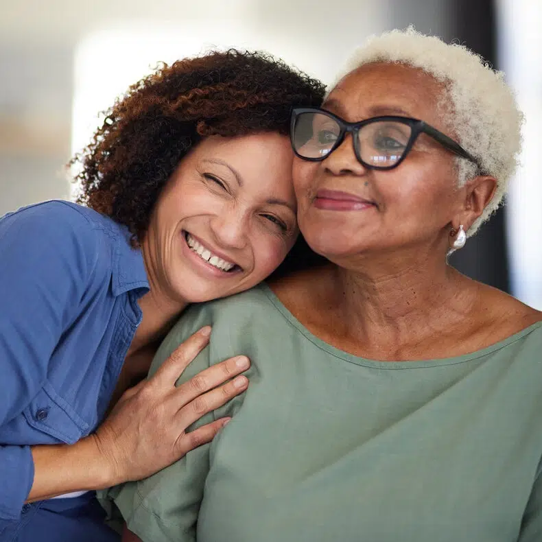 A heartwarming image of a smiling younger woman embracing her content older mother. Both women exude joy and affection in a close, intimate moment, bathed in soft, natural light.
